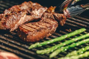 steaks and asparagus cooking on a grill