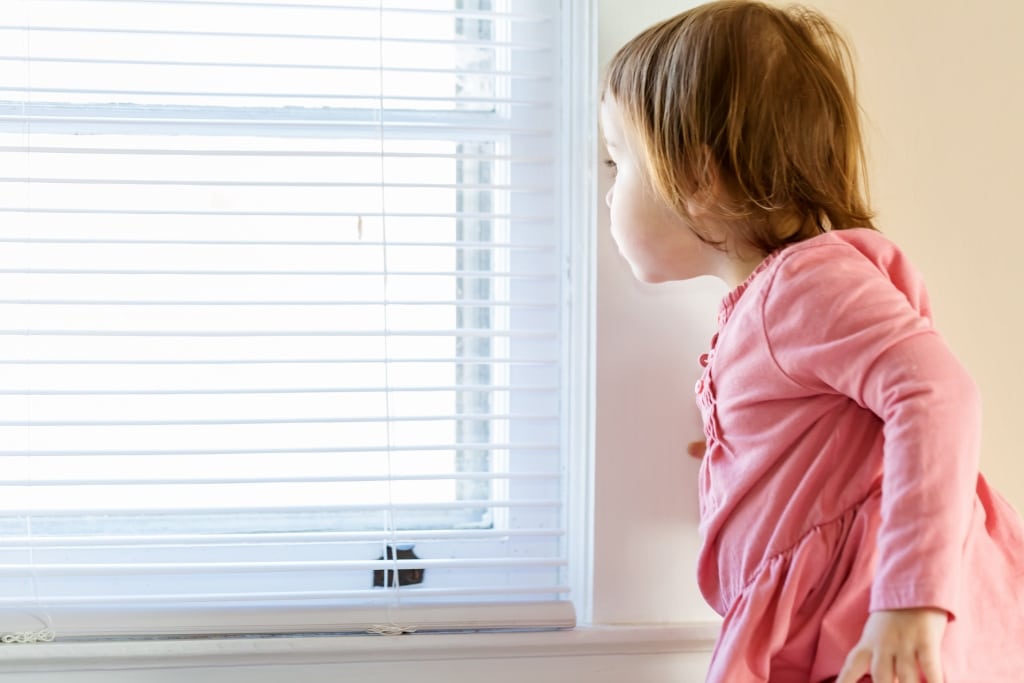 Toddler girl peeking out of the window in her house